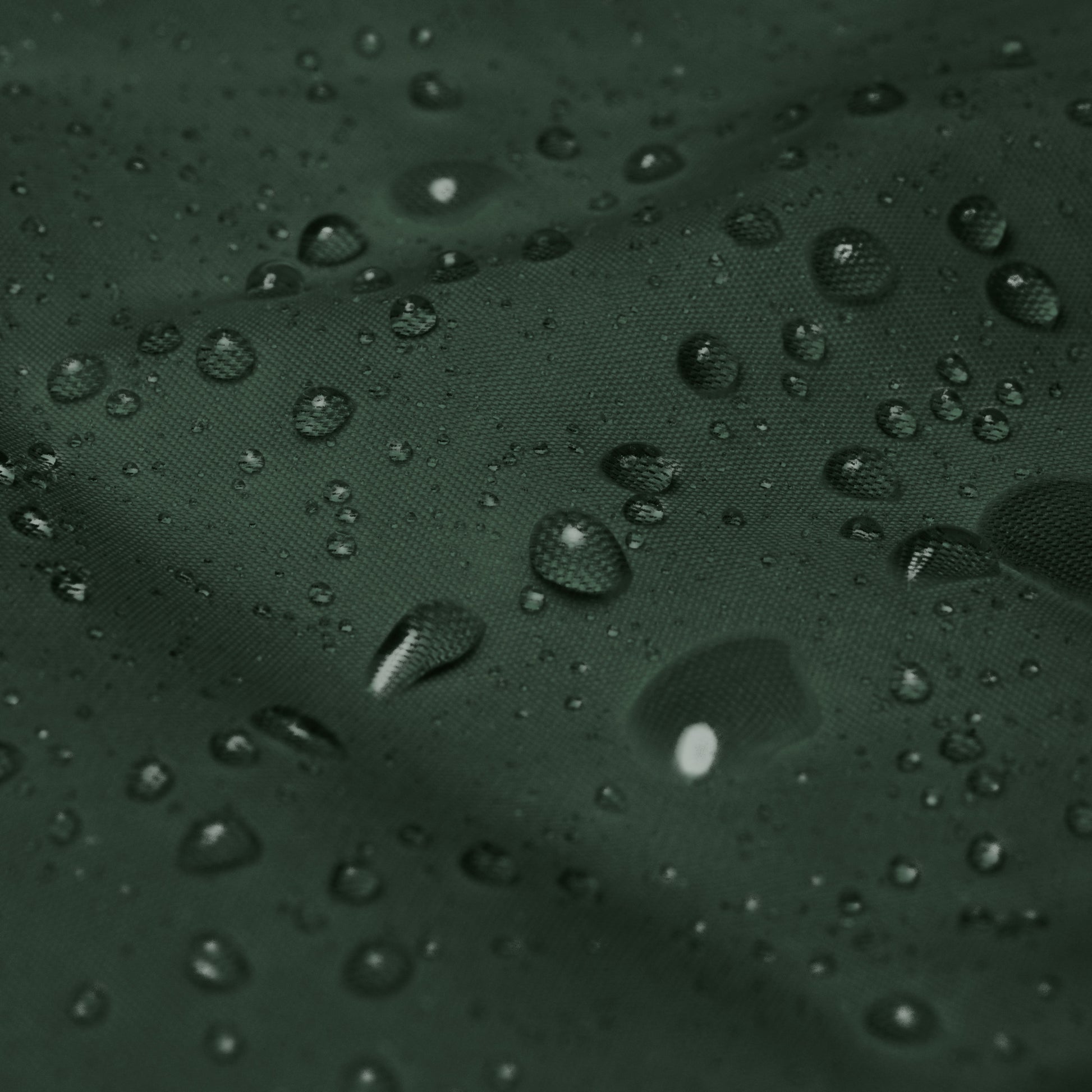 Detalle del tejido impermeable del cortavientos KÖNE verde oscuro con gotas de agua.