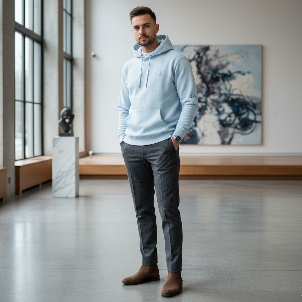 Hombre con sudadera KÖNE blanca y pantalón oscuro, en espacio interior luminoso, estilo urbano elegante.